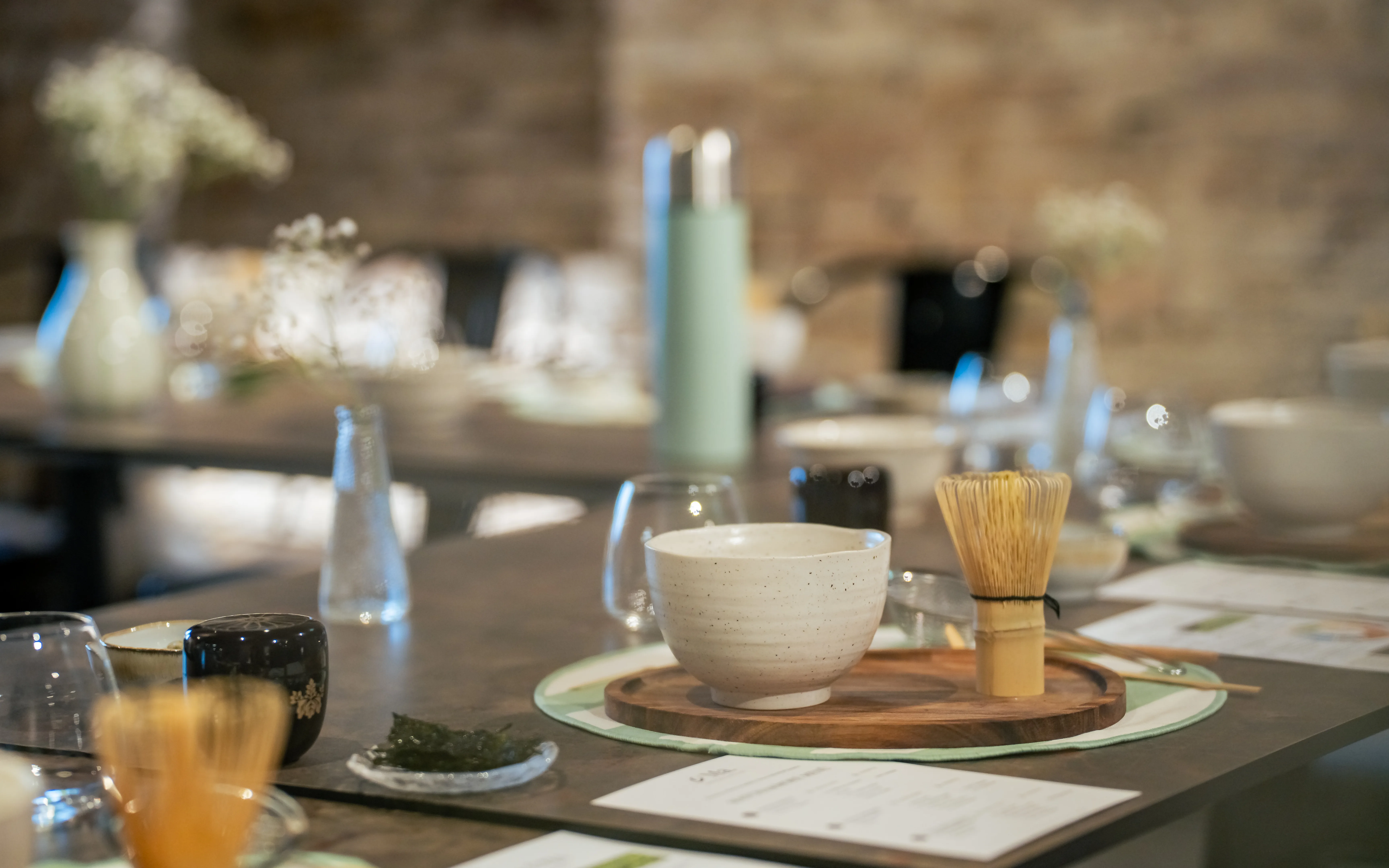 Matcha bowls, bamboo whisks, and ceramic natsume containers set at each place along the workshop table