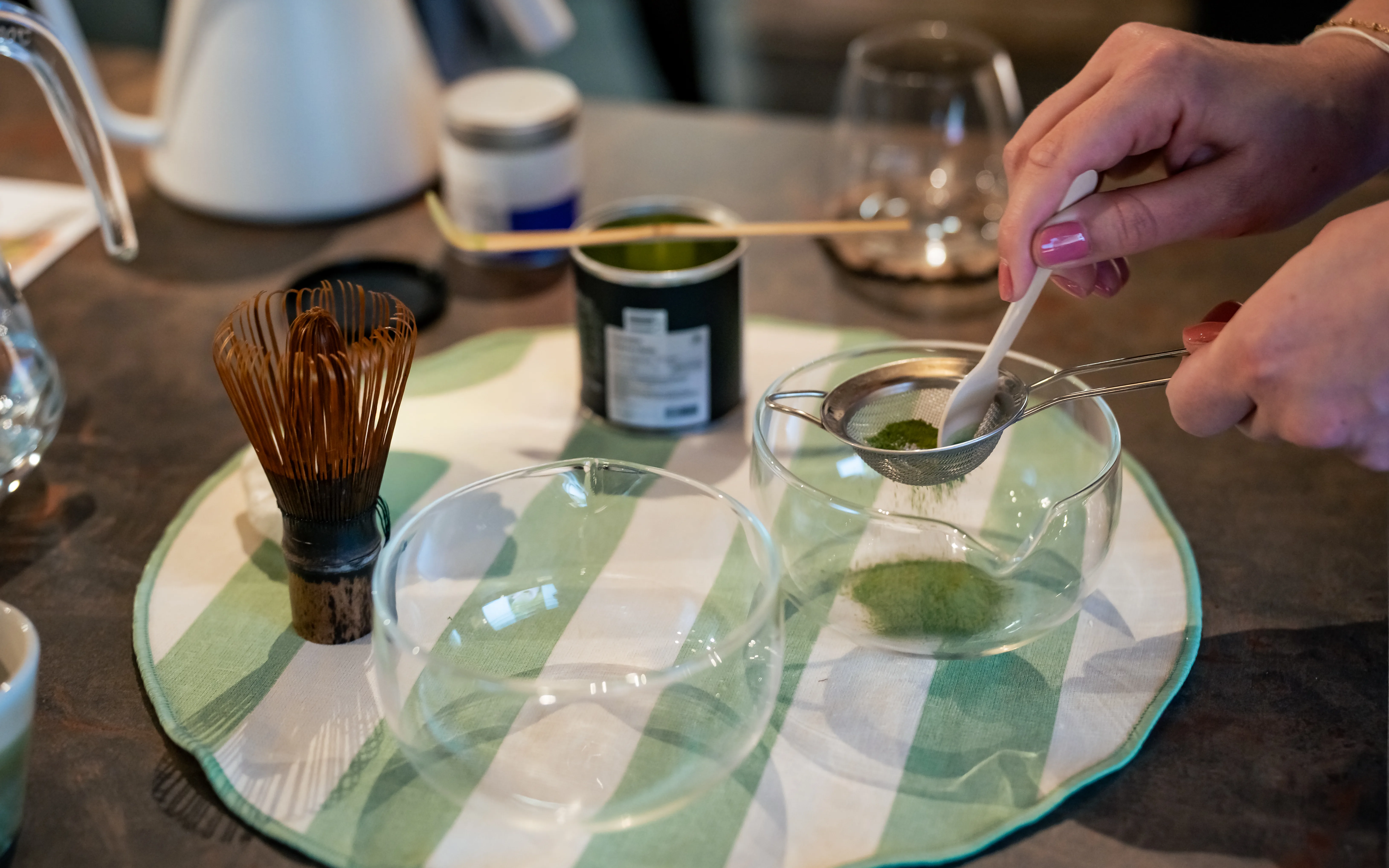 Close-up: vivid green matcha powder beside roasted edamame beans and the decorated lacquer lid of a natsume — the three elements of the tasting