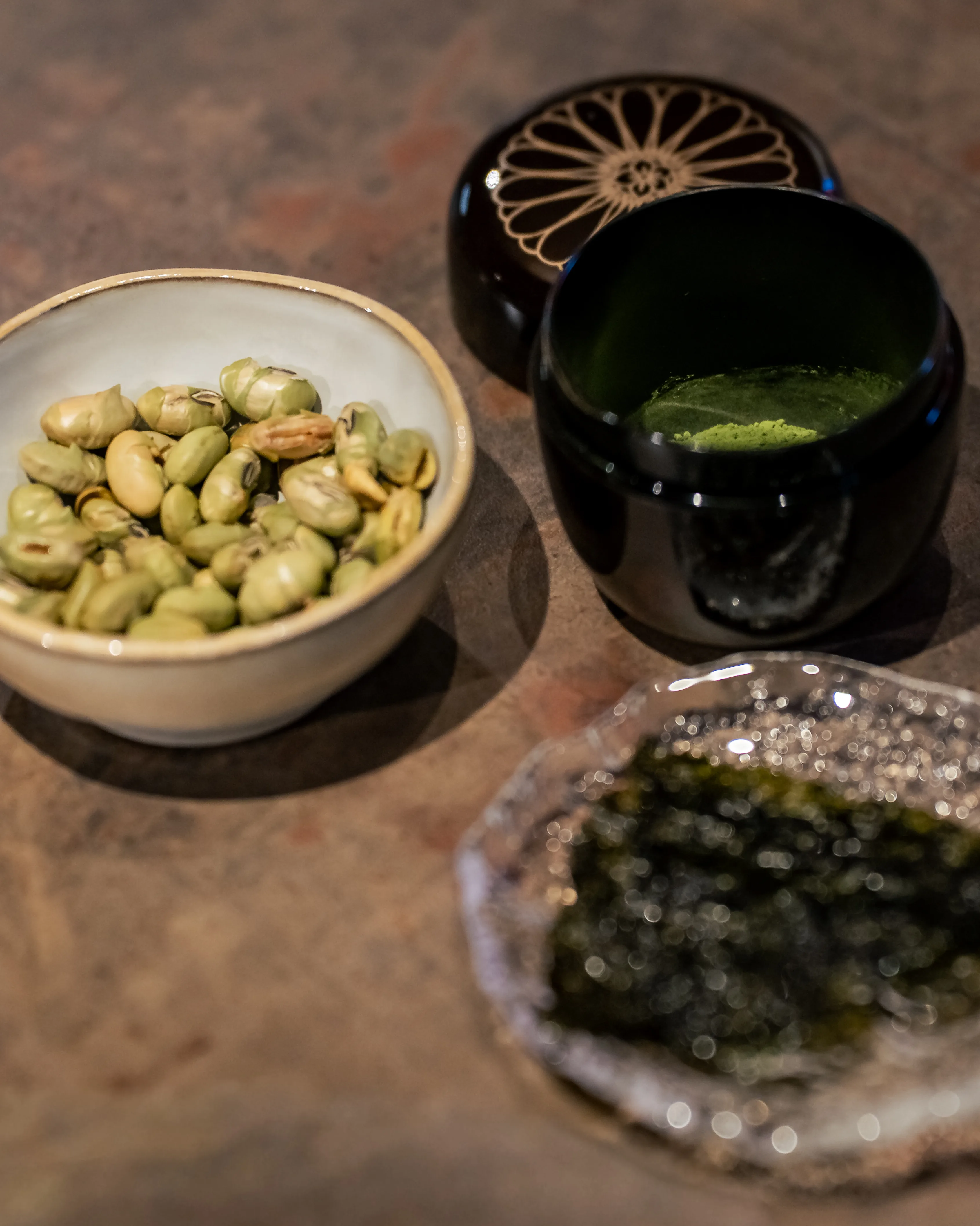 A participant sifts matcha powder through a strainer into a white ceramic chawan bowl held steady on a wooden board