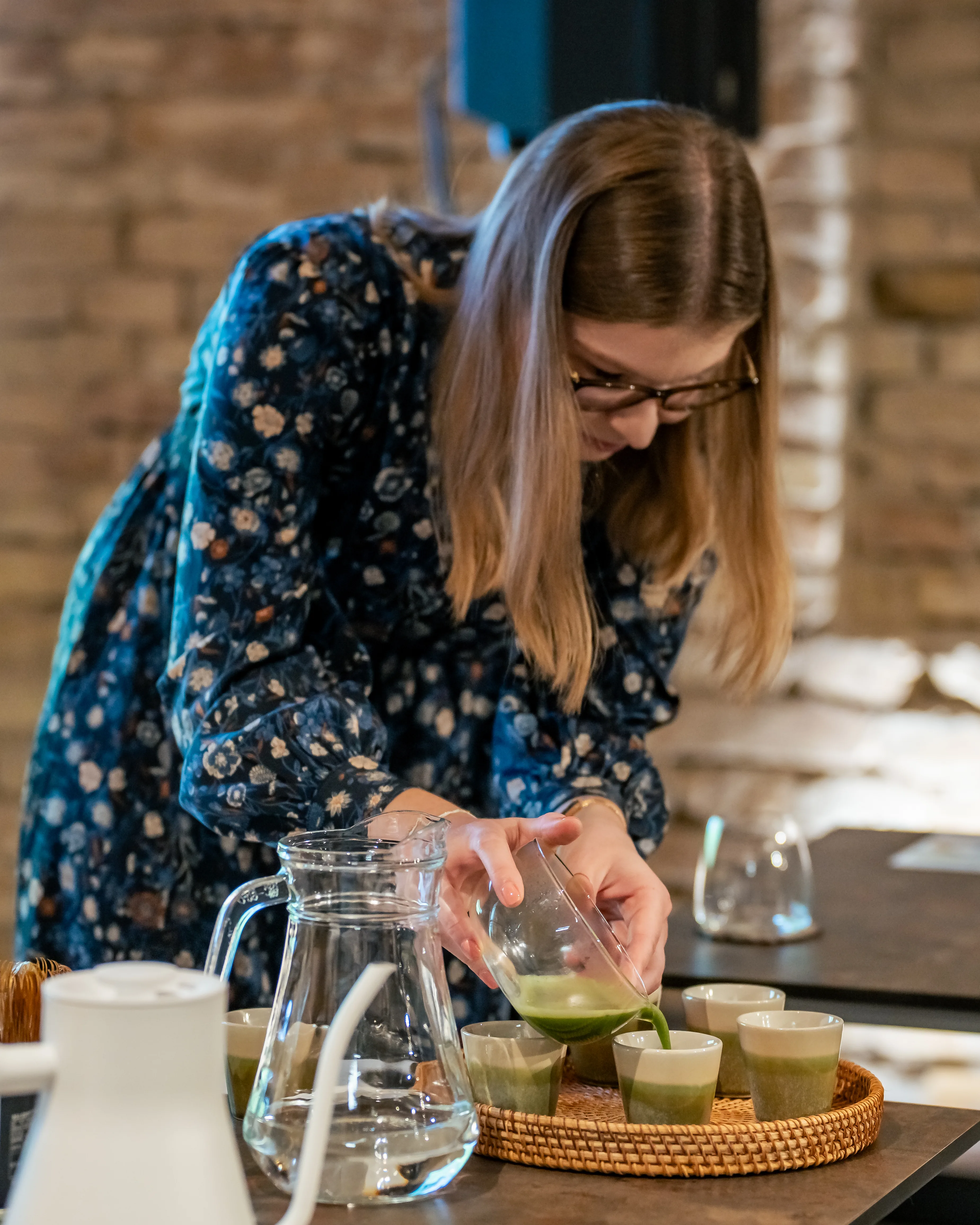 Franciska Nagy pours concentrated matcha into small ceramic tasting cups arranged on a rattan tray