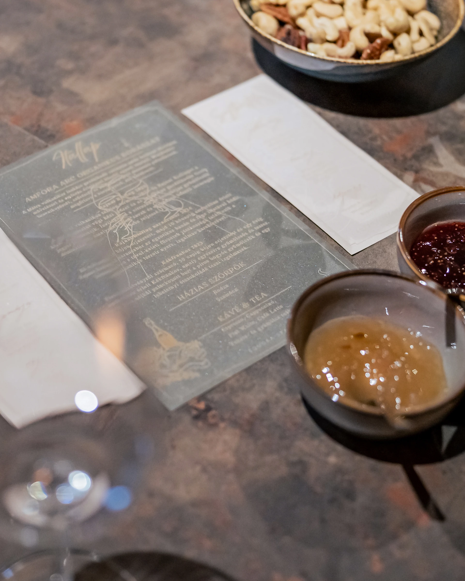 The drinks card of the evening engraved on frosted acrylic, beside a bowl of nuts and two small bowls of fruit preserves
