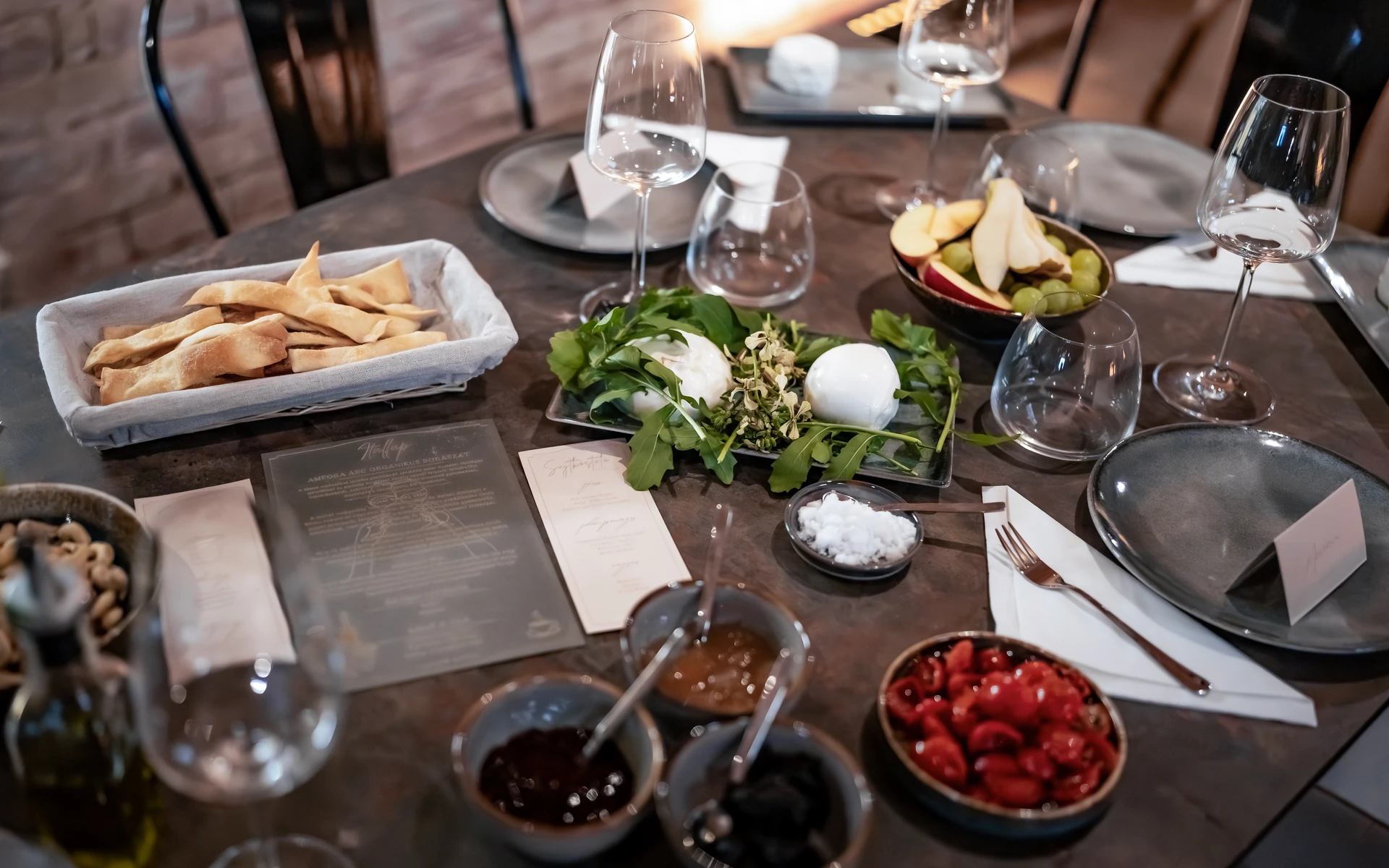 A place set for the tasting: burrata on rocket, bread crisps, sliced apple, pear and grapes, small bowls of preserves and the evening’s cards